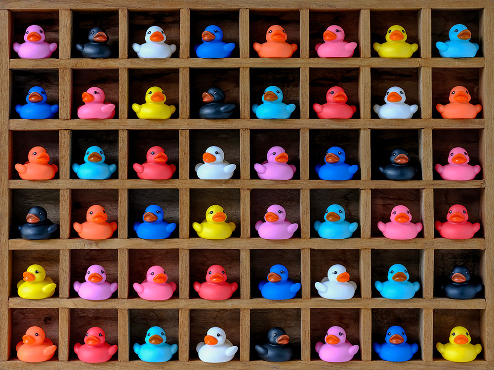 Many multi-colored rubber ducks in wood pigeon hole compartments.